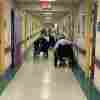 Three people in wheelchairs walk down the hallway of a nursing home. 